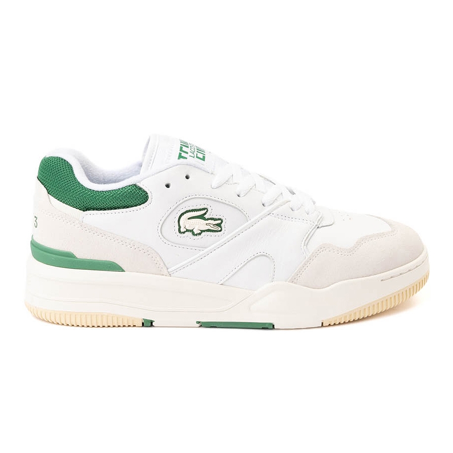 White low-top sneakers feature a green crocodile logo on the side and green accents on the heel, tongue, and sole. They have a leather upper with suede details, a chunky sole, and classic lacing.