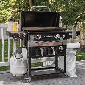 A Blackstone outdoor griddle with side shelves and a propane tank attached, set up on a patio.