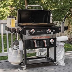 A Blackstone outdoor griddle with side shelves and a propane tank attached, set up on a patio.