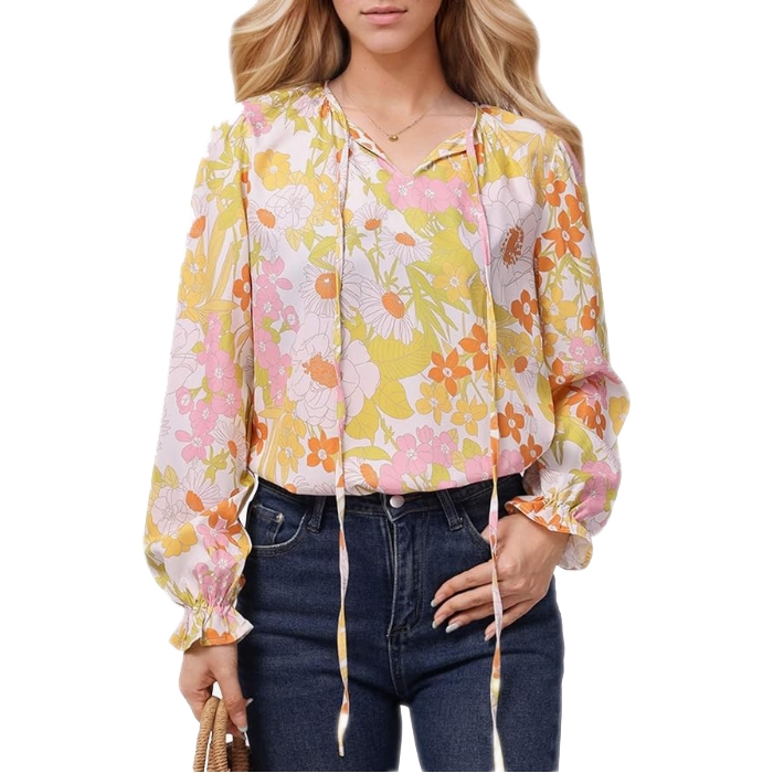 A woman is wearing a floral-print blouse with long sleeves and ribbon ties, paired with dark jeans. The top features pink, yellow, and orange flowers.