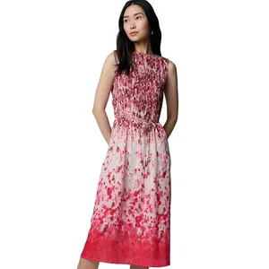 A woman is wearing a sleeveless, knee-length dress with a red and white floral pattern and smocked upper bodice.