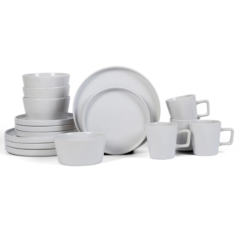 A set of white ceramic dishes including bowls, plates, and mugs with handles, displayed in a neat arrangement.