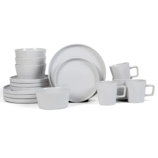A set of white ceramic dishes including bowls, plates, and mugs with handles, displayed in a neat arrangement.
