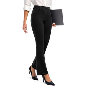 A person wearing a white blouse, black dress pants with flared hems, and black high-heeled shoes, while holding a laptop closed at their side.