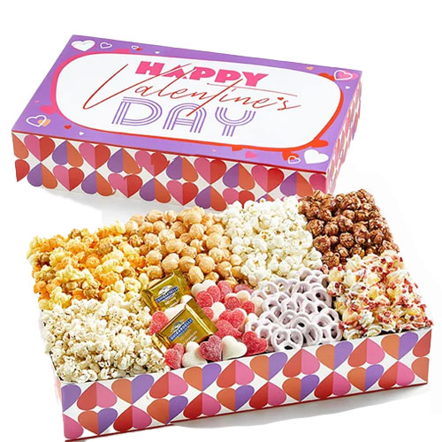 A pink, heart-printed gift box with various popcorn, chocolate, and candy snacks.