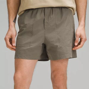 Olive green twill shorts with a 5-inch inseam, designed with a flat front and side pockets, worn by a person with part of a beige shirt visible.