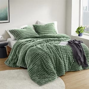 A green ribbed comforter set with matching shams and a decorative grey throw blanket on a bed, set against a neutral room decor.