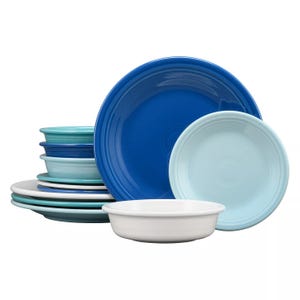 A collection of ceramic dinnerware in various shades of blue and white, including plates and bowls, featuring a simple, ridged design.