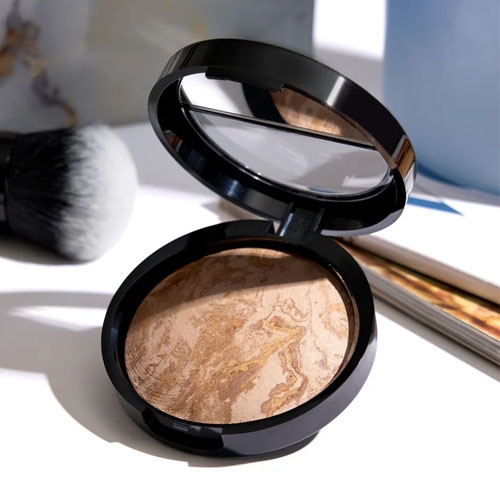 A compact bronzer with a marbled design, accompanied by a makeup brush and mirror inside its lid.