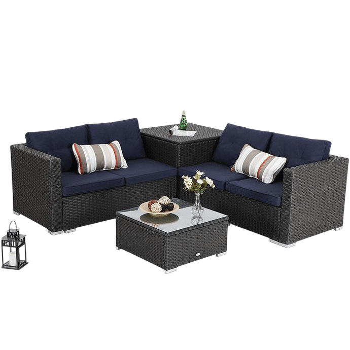 Outdoor sectional furniture set with dark wicker frame, navy cushions, and striped pillows includes a corner table with a glass top and a matching square coffee table. A decorative lantern and floral vase are on the tables.