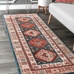 A decorative area rug with a traditional Persian-style pattern featuring blue, red, and cream colors, placed on a dark wood floor next to a gray sofa and white furniture.