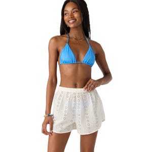 Woman wearing a blue bikini top and white eyelet shorts, accessorized with bracelets and necklaces.