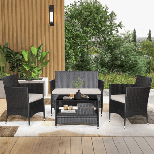 Outdoor patio set featuring a 2-tier table, a loveseat, and two armchairs with black wicker frames and light cushions, set on a patterned rug. Lush greenery and wood siding provide a calming backdrop.