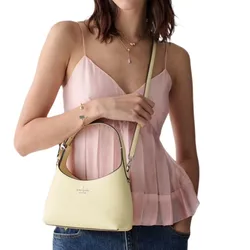 A woman in a pink sleeveless top and jeans holds a light yellow Kate Spade crossbody bag with a top handle.