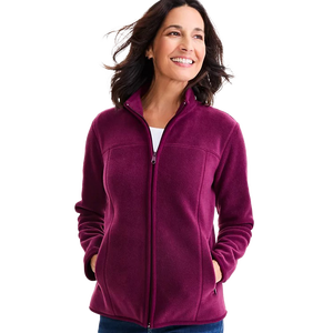 A woman is wearing a magenta fleece zip-up jacket with a high collar and pockets, paired with a white top and blue jeans.