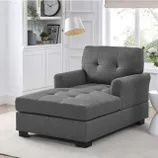 A gray chair with a tufted seat and back cushion, and black feet, in a bright room.