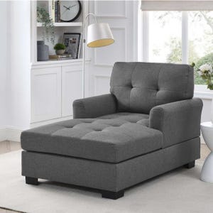 A gray chair with a tufted seat and back cushion, and black feet, in a bright room.