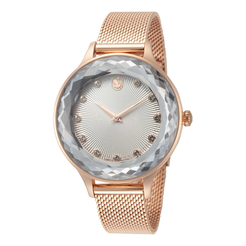 A rose gold watch with a mesh band features a faceted crystal bezel, sunburst dial, and crystal hour markers.