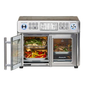 A stainless steel French door toaster oven with digital controls displays various cooking modes like air fry, roast, and grill. It's shown with food inside, including vegetables and meat, across two compartments for separate simultaneous cooking.
