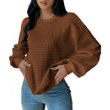 A person wears a brown, textured waffle-knit sweater paired with blue jeans.