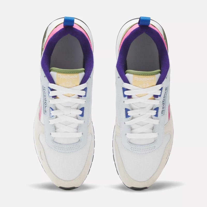 A pair of white sneakers with colorful accents on the tongue, heel, and sides. They feature a lace-up design and branding on the insoles.