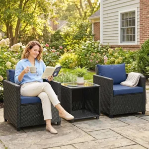 Outdoor patio conversation set featuring two wicker chairs with blue cushions, a side table with a glass top, and a woman enjoying a book and drink.