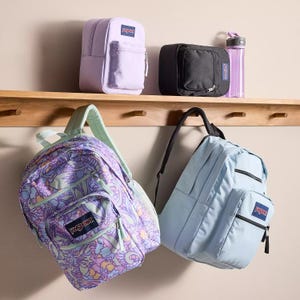 Four backpacks displayed on pegs: a lavender pouch, a black pouch with water bottle, a purple patterned backpack, and a light blue backpack.