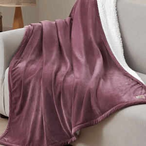 UGG Dasha Plush Throw features a soft plum-colored exterior and a cozy white sherpa lining, draped over a light-colored couch.