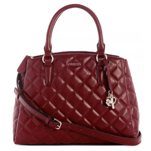 A red quilted handbag with two top handles, a detachable shoulder strap, and decorative charms. It features the GUESS logo on the front.