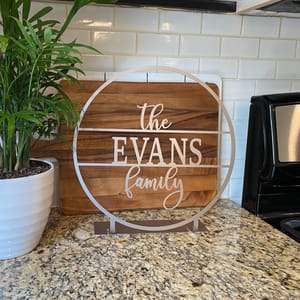 The tabletop name sign is a circular wooden piece with a metal structure outlining the edges, displaying \“The EVANS family\“ in a script font.