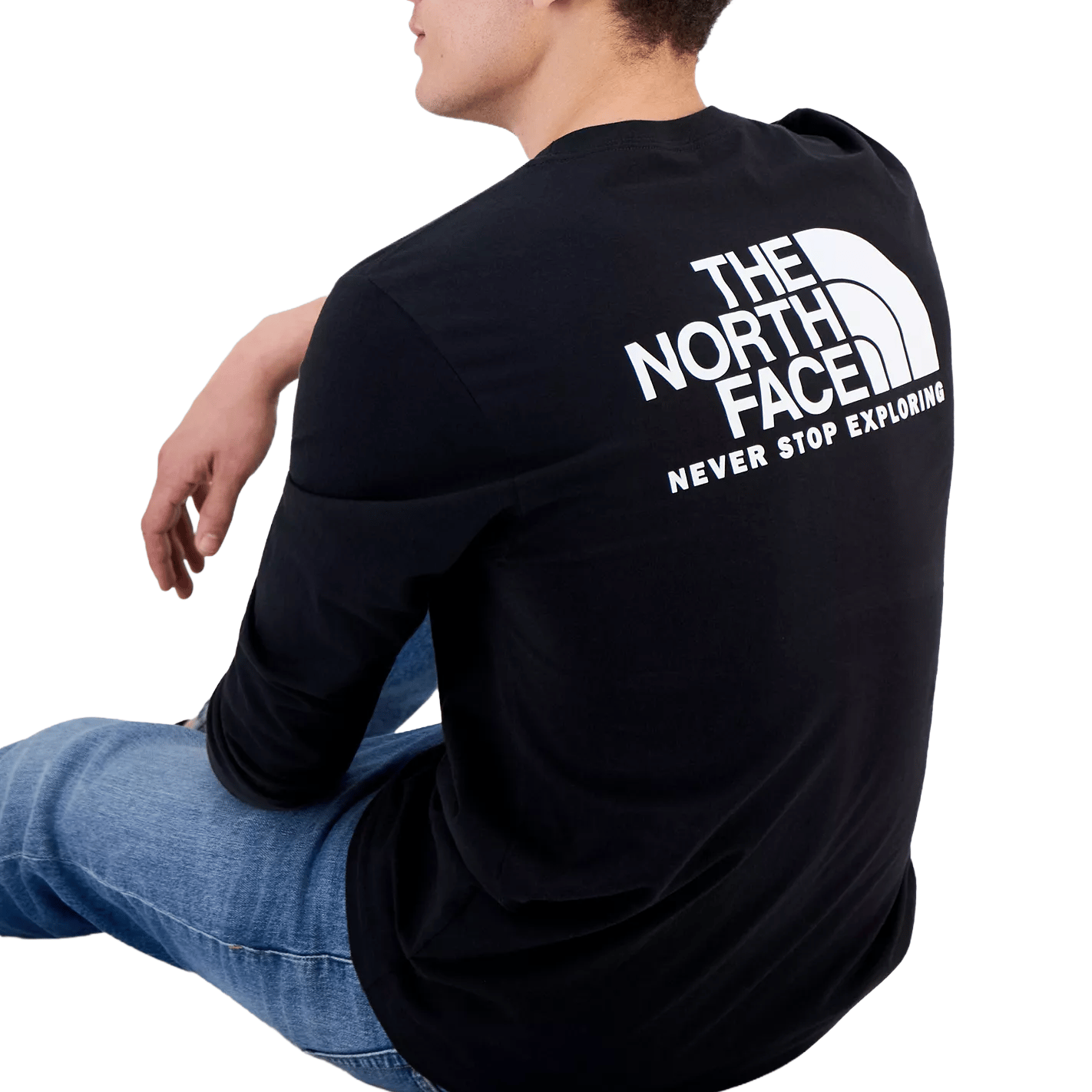 A person wearing a black long-sleeve The North Face shirt with the text \“NEVER STOP EXPLORING\“ on the back, paired with blue jeans.