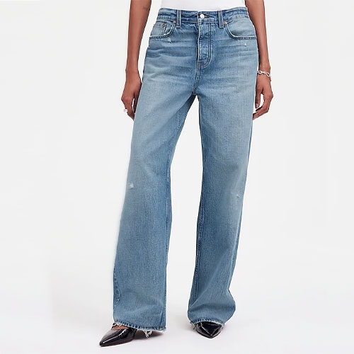 a pair of loose-fit jeans in a medium blue wash on a person wearing black pointy toe flats and a white shirt