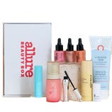 A collection of beauty products including a Tula cleanser, body wash, brow pencil, hair care products, illuminator pigments, and Ultra Repair Cream, accompanied by an Allure Beauty Box.