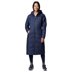 A woman is wearing a long, navy-blue quilted coat with a hood, paired with dark leggings and athletic shoes. The coat has a full-length zipper and appears insulated for warmth.