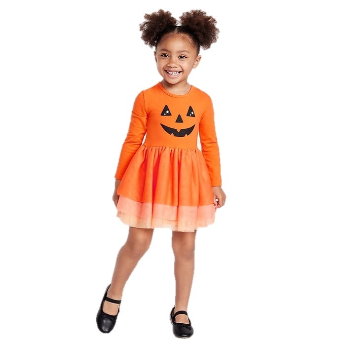 Young girl in a pumpkin-themed orange dress with a jack-o'-lantern face on the front, wearing black shoes.