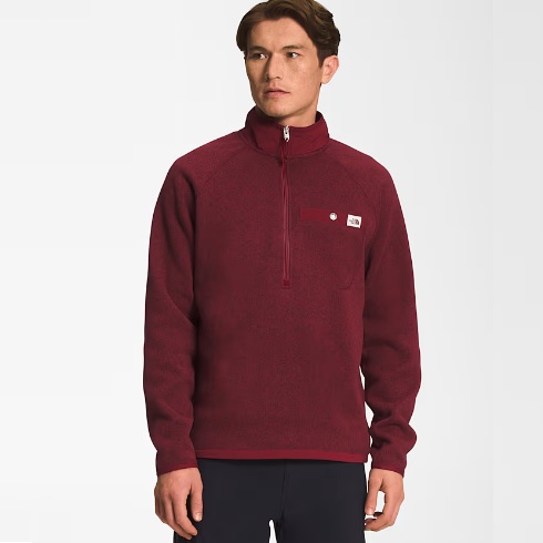 A man is wearing a maroon fleece pullover with a half-zip collar and a small white logo on the chest.