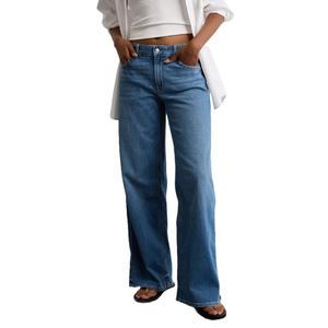 A person wears blue high-waisted flared jeans paired with a white crop top, a white shirt, and black sandals.