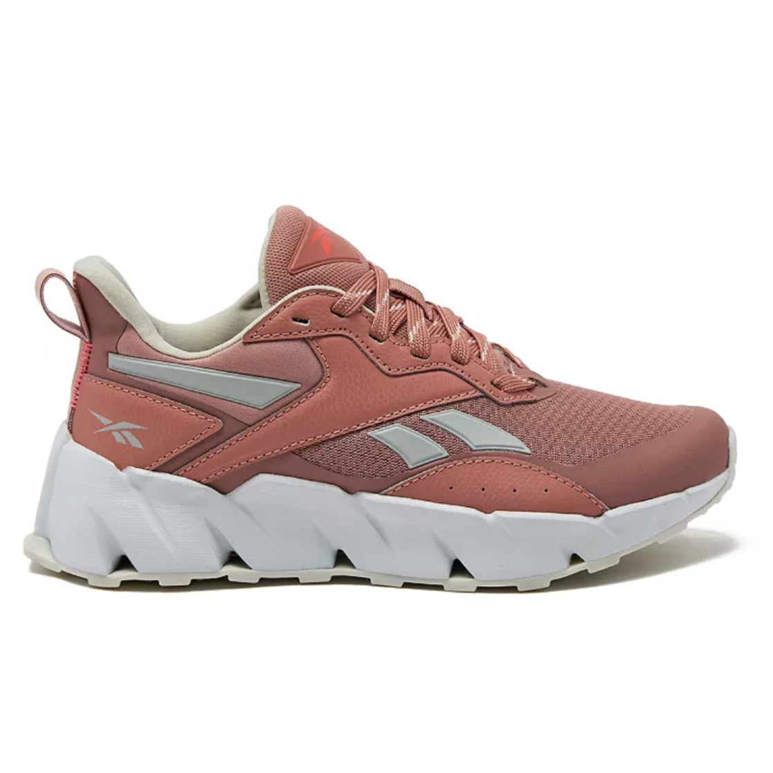 A pink Reebok sneaker with a white, chunky zigzag sole and gray logo accents on the side, featuring a lace-up design and a pull tab on the heel.