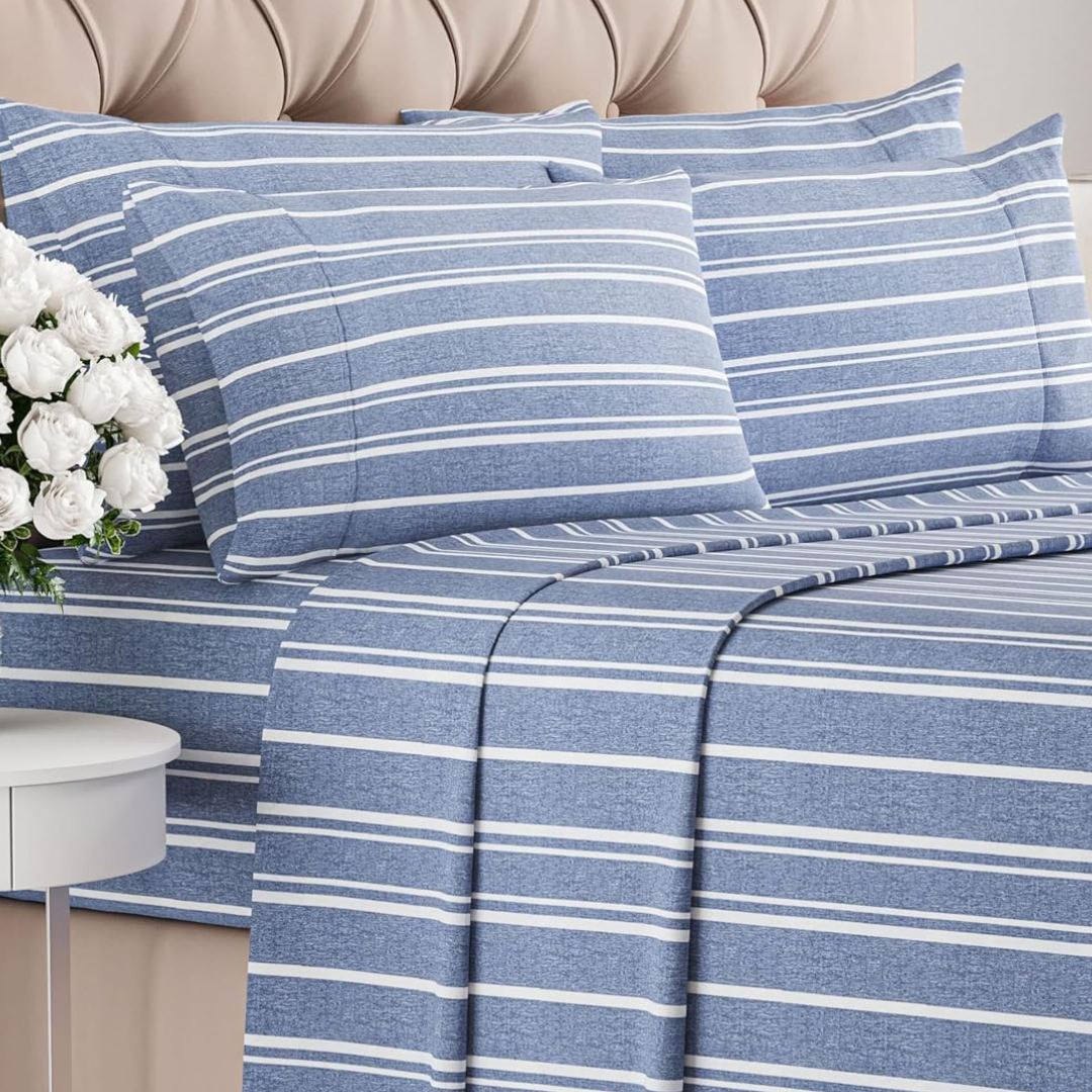 Blue striped 6-piece cooling sheet set with a soft texture, includes four pillowcases, a fitted sheet, and a flat sheet, displayed on a bed with a tufted headboard and white flowers on a side table.
