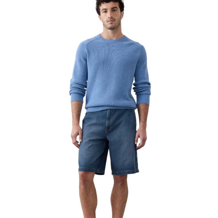 A man is wearing a light blue sweater, denim shorts, and white sneakers.