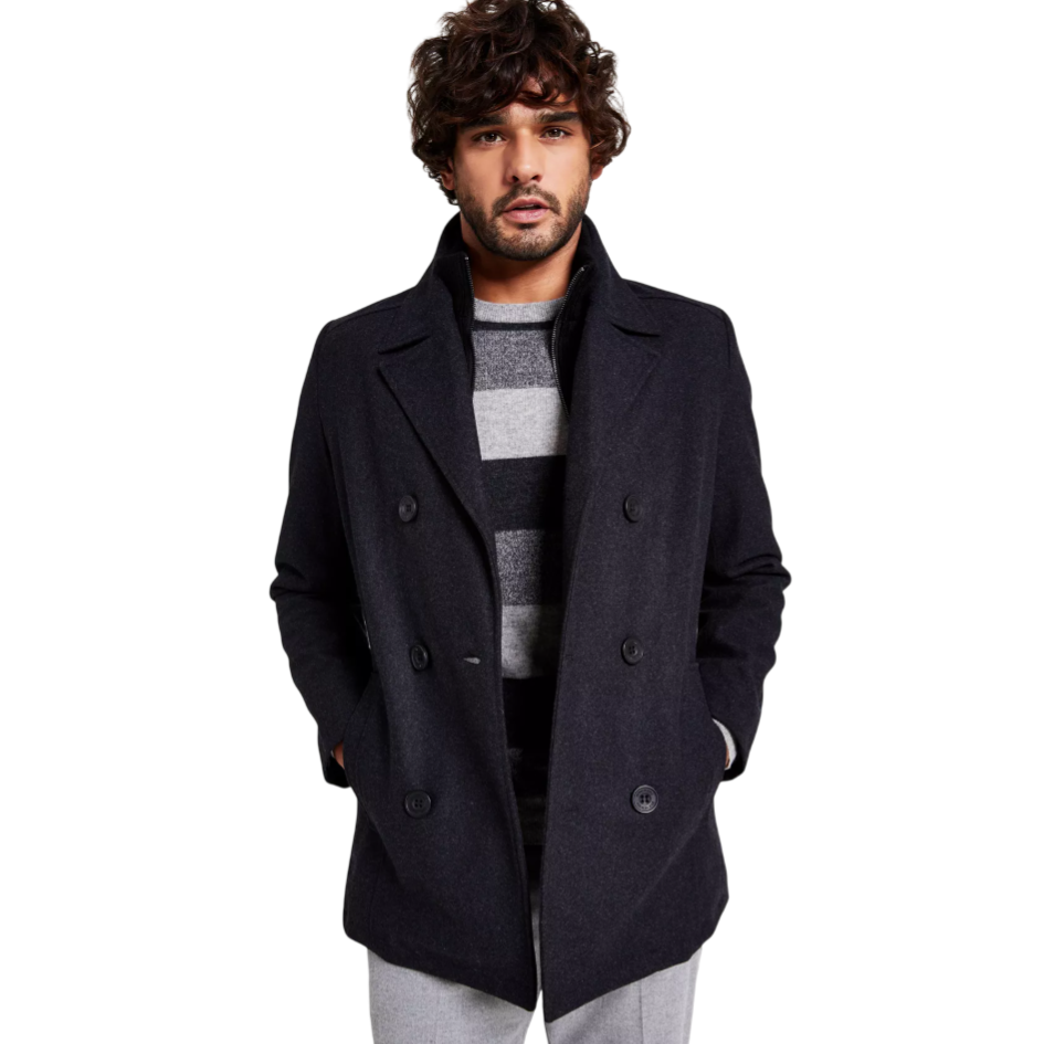 A man is wearing a dark double-breasted coat over a gray and black striped sweater, paired with light gray pants.