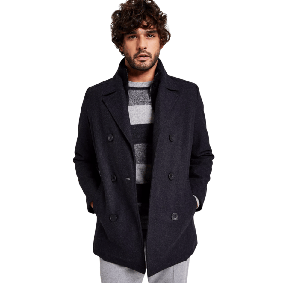 A man is wearing a dark double-breasted coat over a gray and black striped sweater, paired with light gray pants.