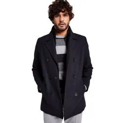 A man is wearing a dark double-breasted coat over a gray and black striped sweater, paired with light gray pants.