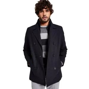 A man is wearing a dark double-breasted coat over a gray and black striped sweater, paired with light gray pants.