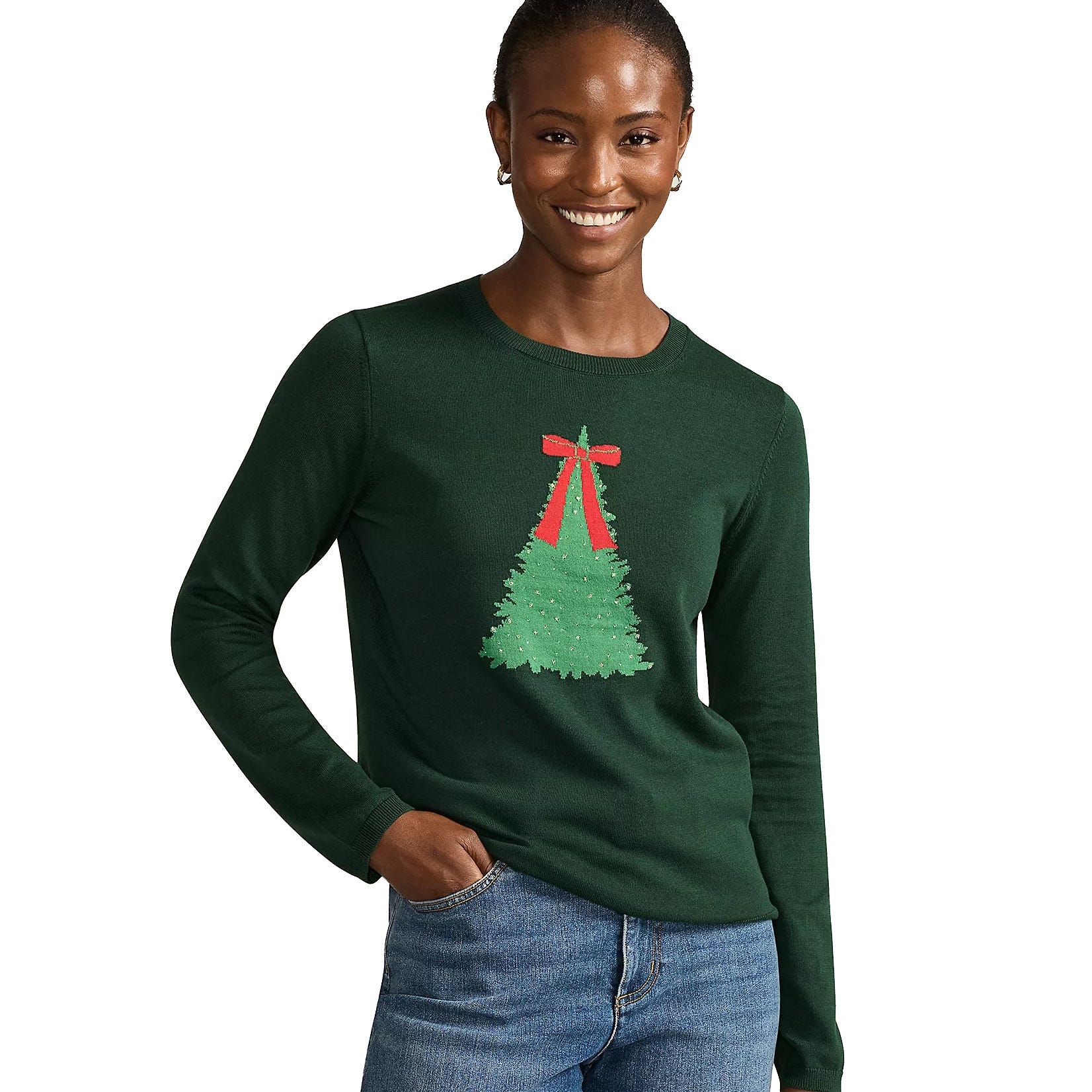 A woman wearing a dark green sweater featuring a Christmas tree design with a red ribbon, paired with blue jeans.