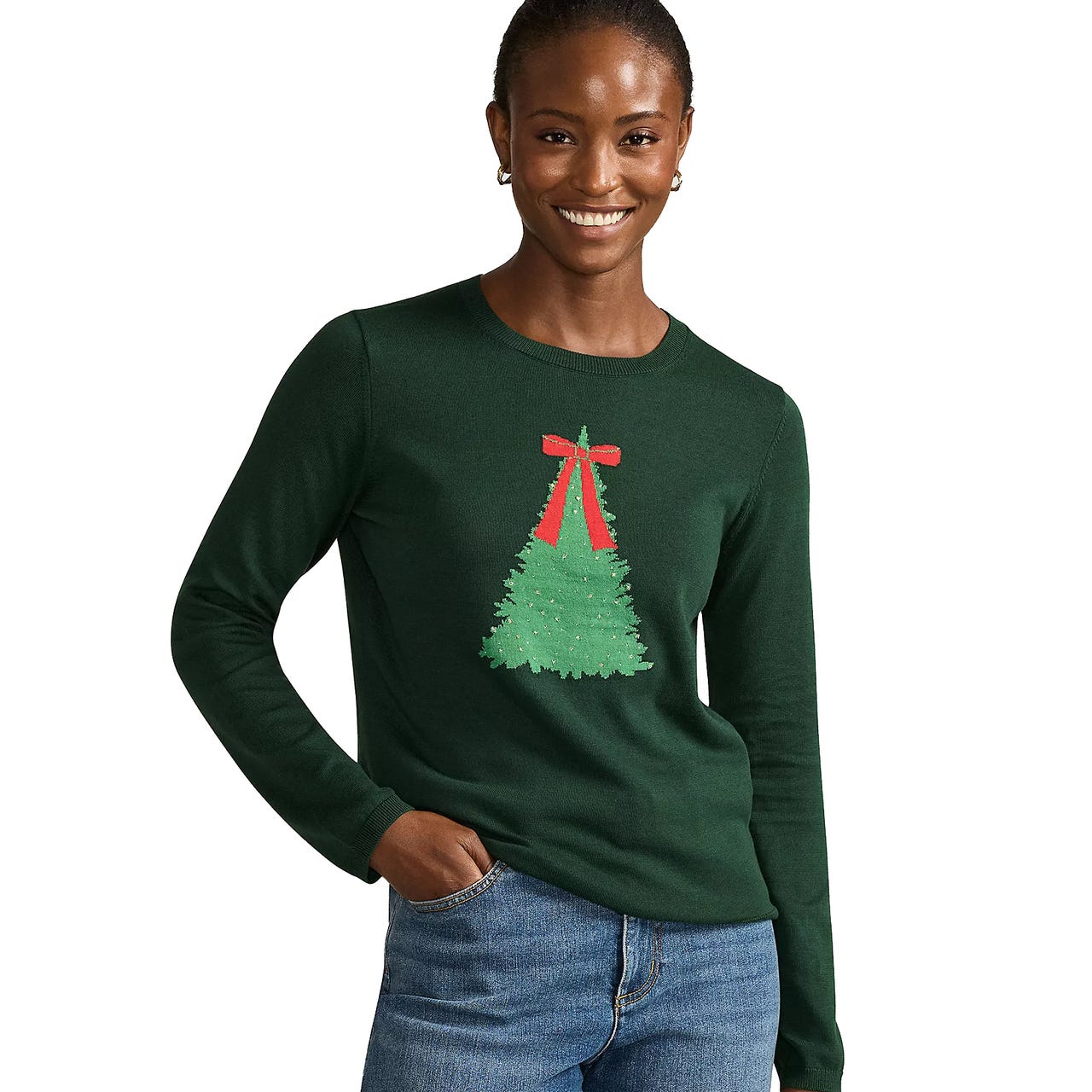 A woman wearing a dark green sweater featuring a Christmas tree design with a red ribbon, paired with blue jeans.