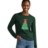 A woman wearing a dark green sweater featuring a Christmas tree design with a red ribbon, paired with blue jeans.