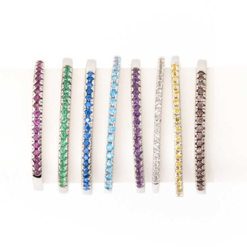 A collection of colorful, thin bracelets featuring different gemstones in hues of purple, green, blue, aqua, purple, white, yellow, and brown, set in alternating silver bands.