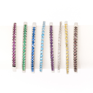 A collection of colorful, thin bracelets featuring different gemstones in hues of purple, green, blue, aqua, purple, white, yellow, and brown, set in alternating silver bands.