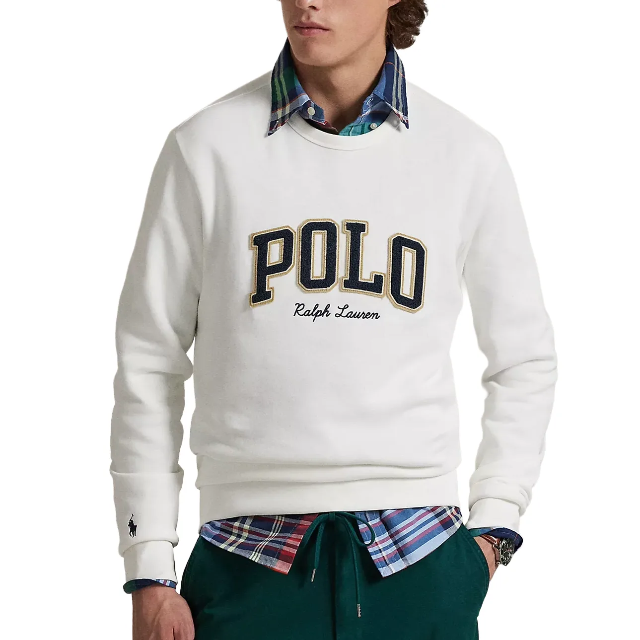 A person wears a white sweater with \“POLO Ralph Lauren\“ embroidered on it, layered over a blue, green, and red plaid button-up shirt. The outfit is completed with green pants.